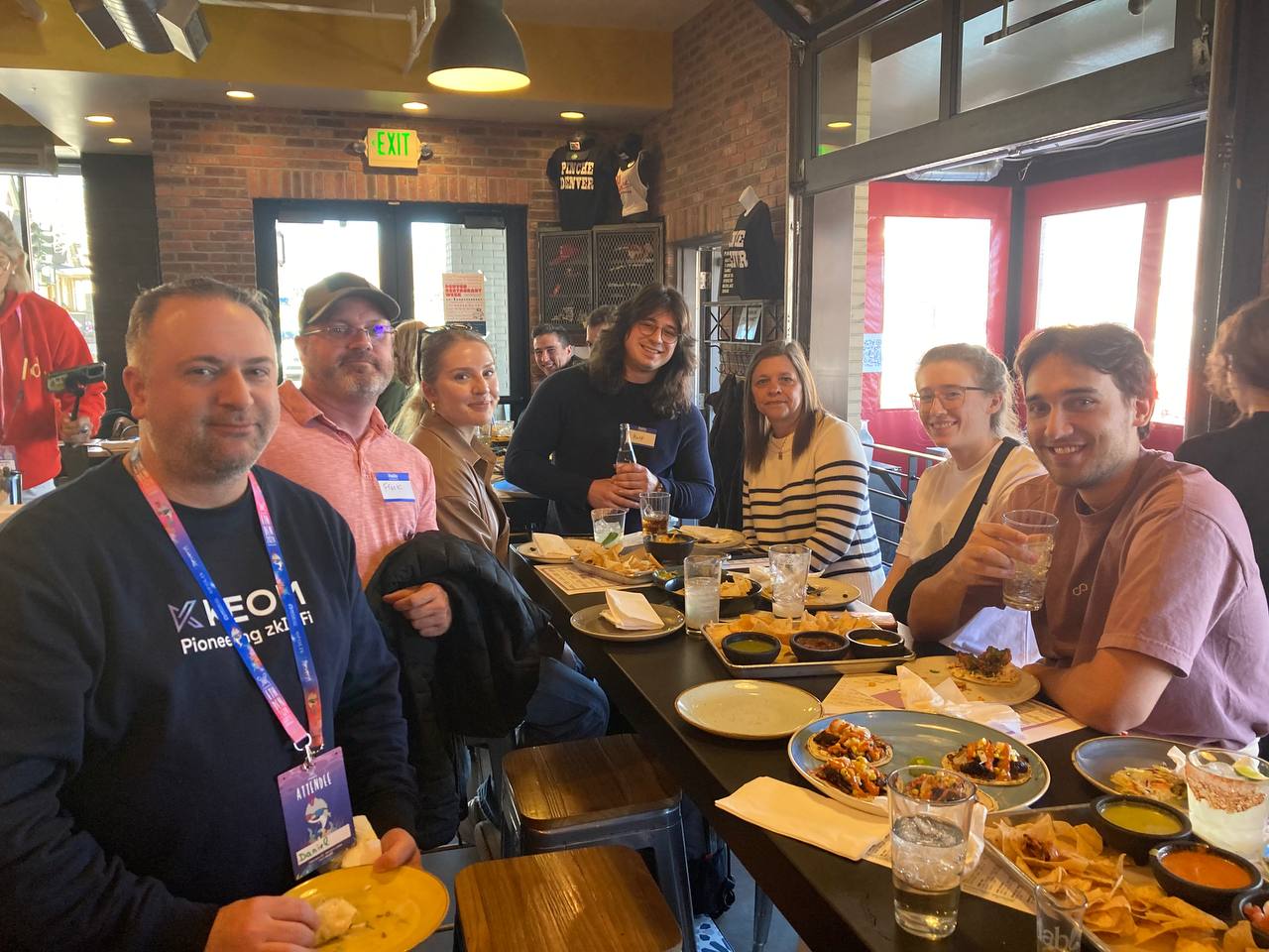 A picture of Dabl.Club attendees around a table of tacos, chips, and drinks.
